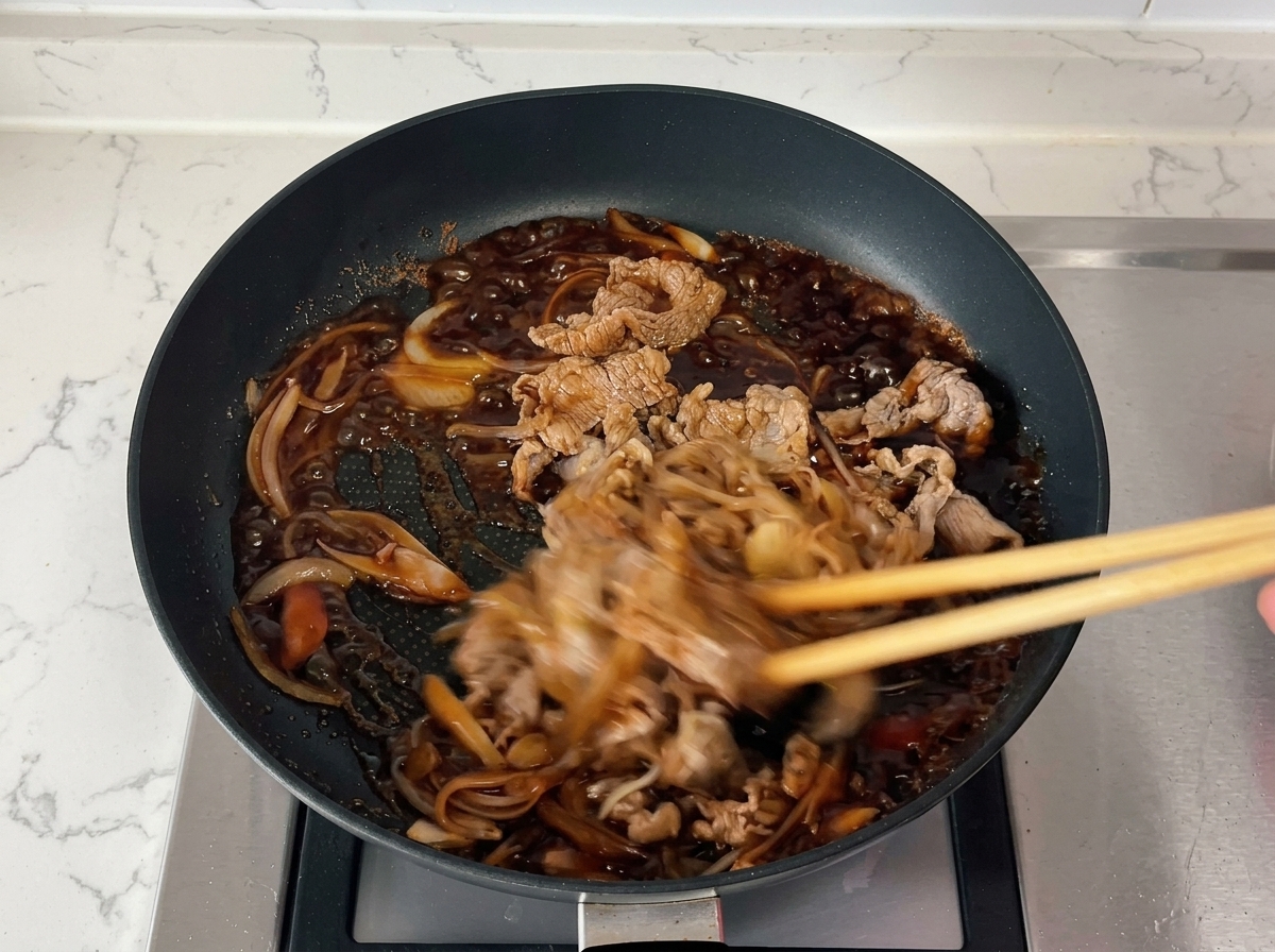 Chopsticks quickly stirring beef and onions in a bubbling, thickened dark sauce.