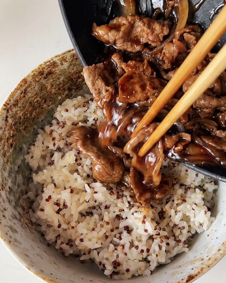 Cooked beef and onions being poured from a pan over a bowl of steamed white rice mixed with quinoa.