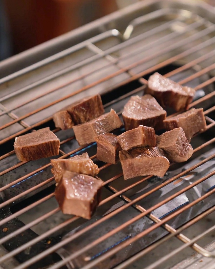 Several thick-cut pieces of beef tongue on a metal grill grate, glistening with a rich, dark brown sauce.