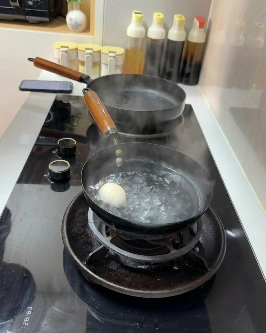 A single white egg submerged in a small pot of rapidly boiling water on a gas stove.