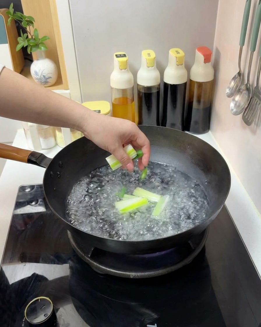 A hand dropping cut pieces of green scallions into a wok of boiling water.