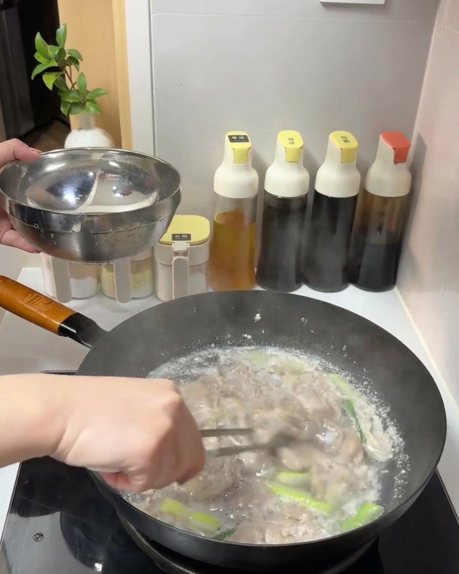 Cooked beef slices being lifted out of a pot of simmering water with tongs into a metal bowl.