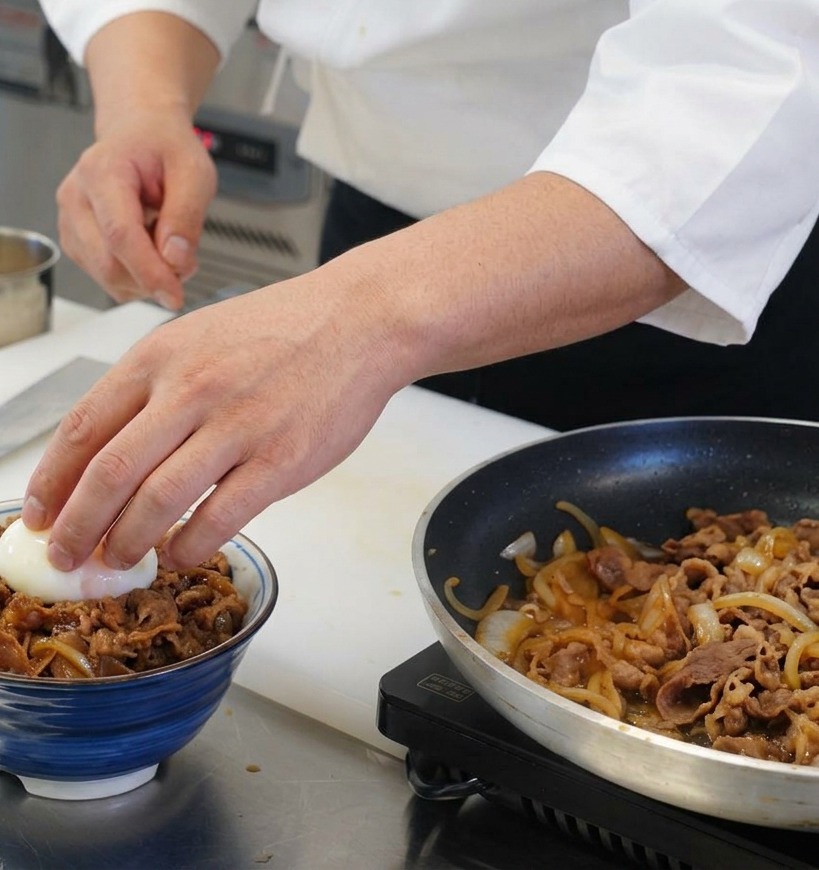 A hand placing a soft boiled egg with a translucent white and orange yolk onto a prepared bowl of beef and rice