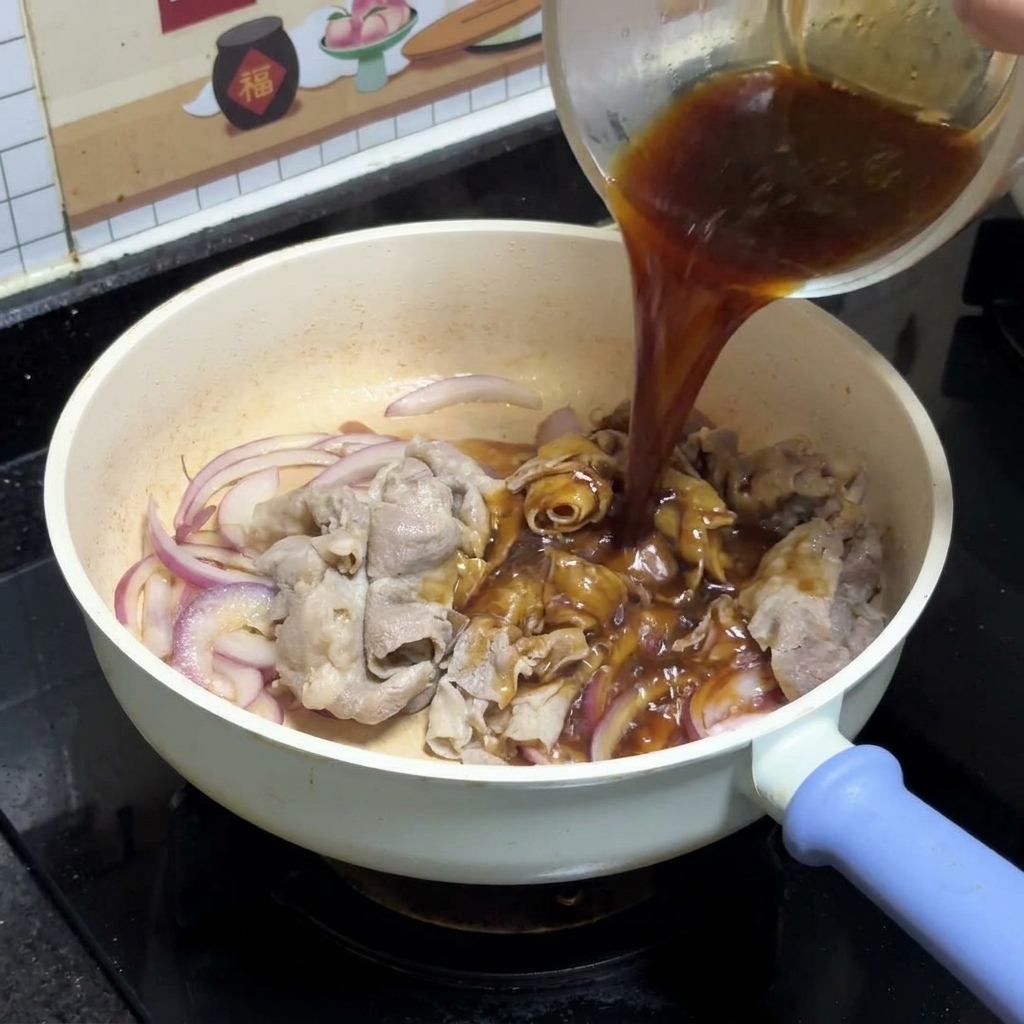 Dark teriyaki sauce being poured from a clear glass bowl over sautéed red onions and beef slices in a white pan.