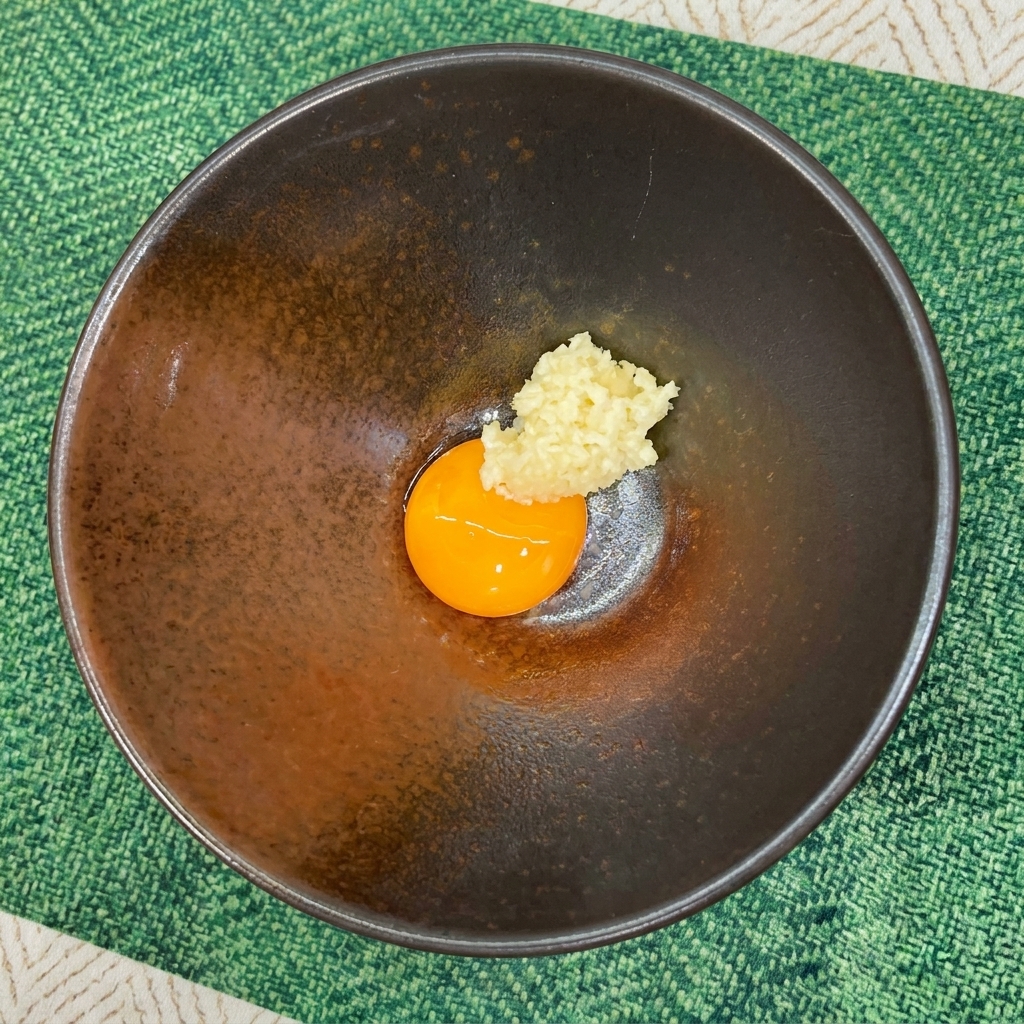 Minced garlic placed directly next to a bright orange raw egg yolk in a dark bowl.