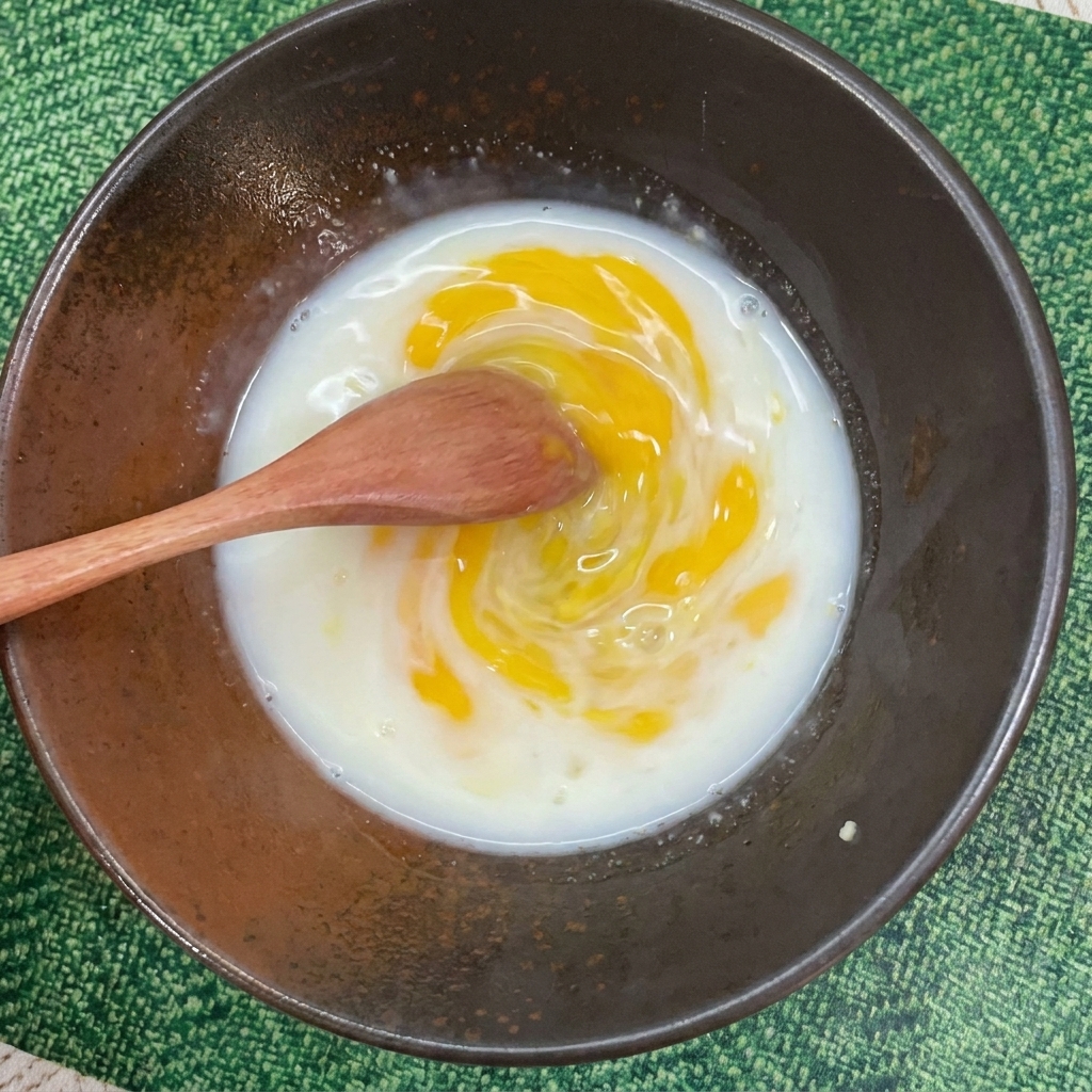 A wooden spoon stirring a milky yellow broth inside a dark ceramic bowl.