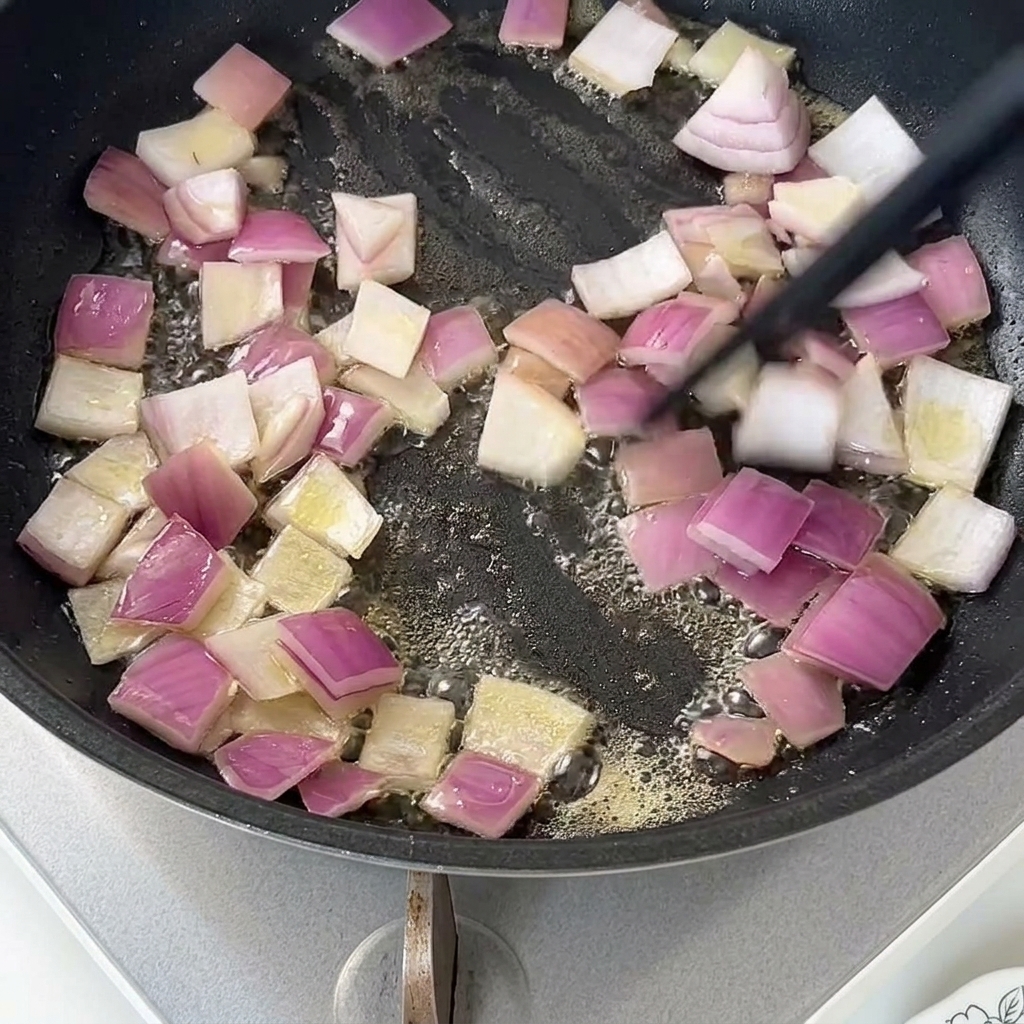 Diced red onions sautéing in melted butter in a dark non-stick pan.