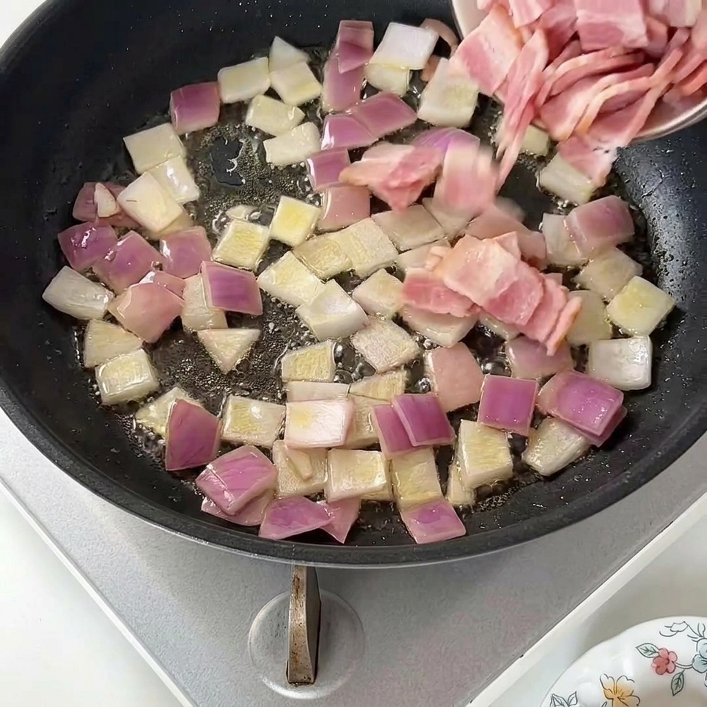 Adding small pieces of raw bacon from a small dish into a pan of sautéed red onions.