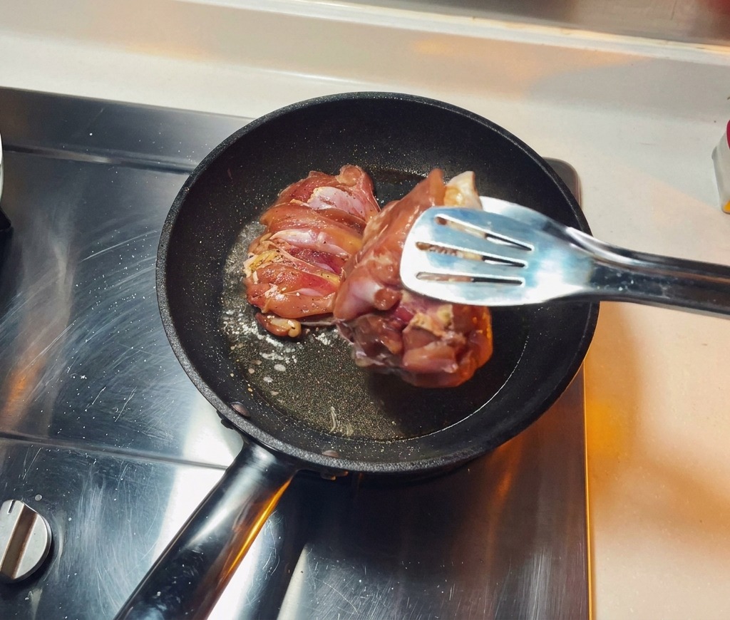 Marinated chicken thighs being placed skin down into a hot frying pan with shimmering oil.