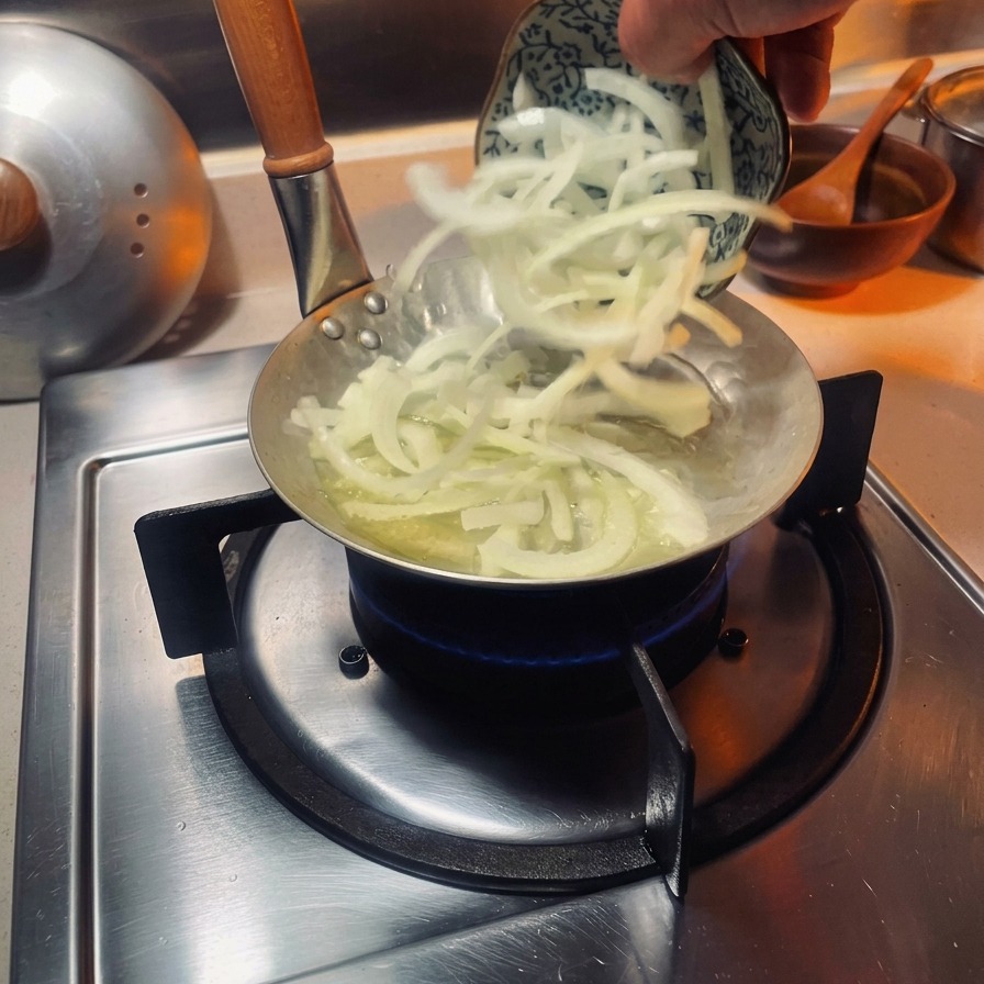 Sliced white onions being added to a small, specialized oyakodon pan over a gas burner.