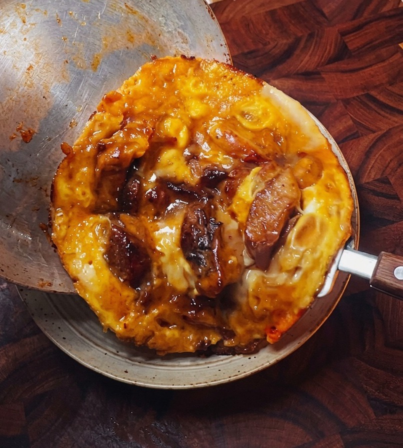The cooked egg and chicken topping being slid from a metal pan onto a bowl of fluffy white rice.