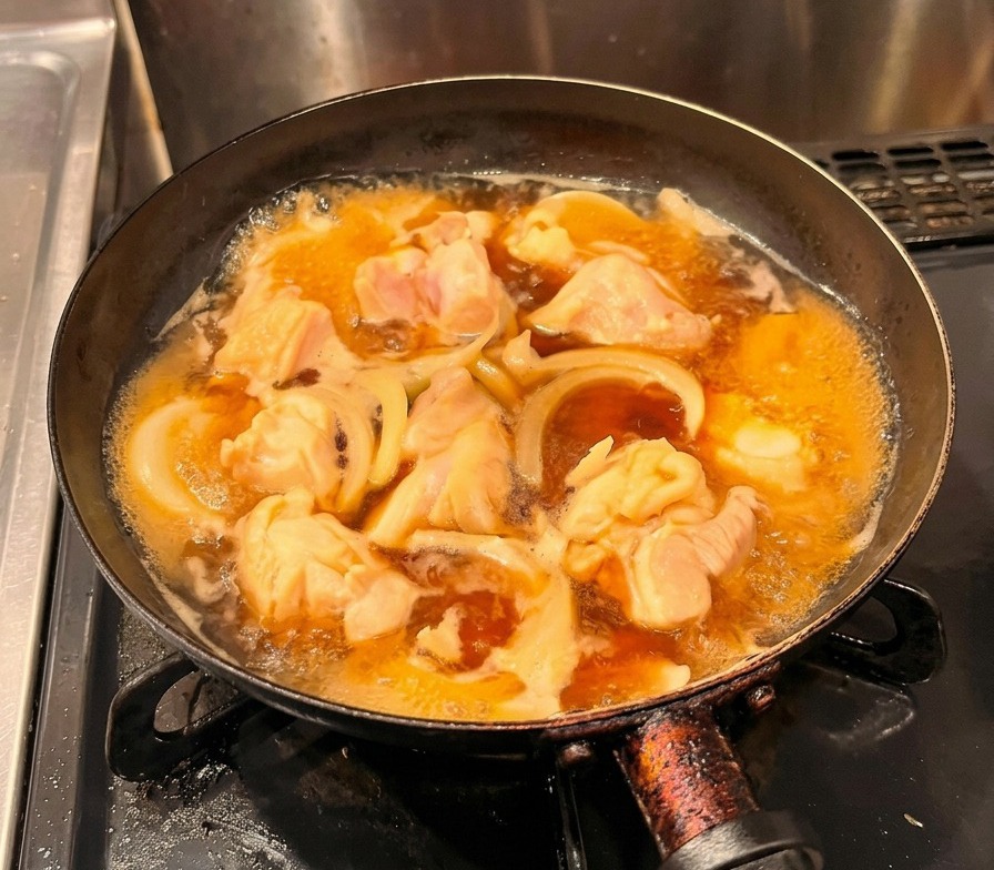 Beaten yellow eggs being poured in a steady stream over simmering chicken and onions in a black pan.