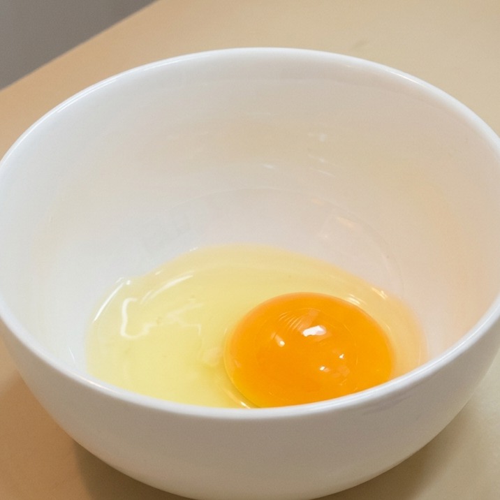 A raw egg yolk and clear white resting in a white ceramic bowl.