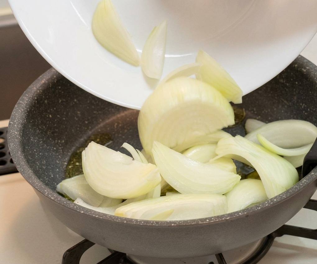Sliced white onion wedges being transferred from a white plate into a gray, non-stick frying pan.