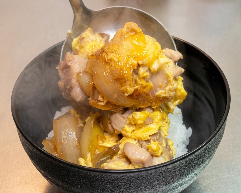 A steaming ladle of Oyakodon being served onto a bowl of fluffy white rice.