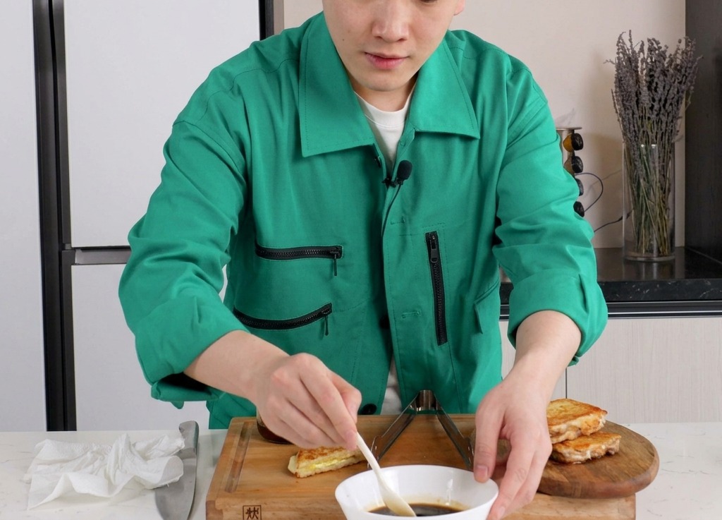 A person stirring a dark brown soy-based sauce in a white ceramic bowl using a small white spoon.