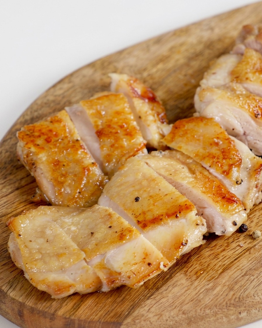 Crispy pan-fried chicken thigh sliced into several uniform pieces on a wooden board.
