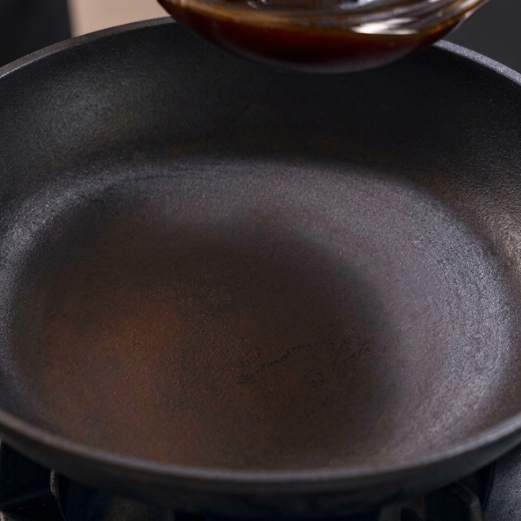 A dark, savory-sweet Oyakodon sauce being poured into a black, seasoned skillet over a stove.