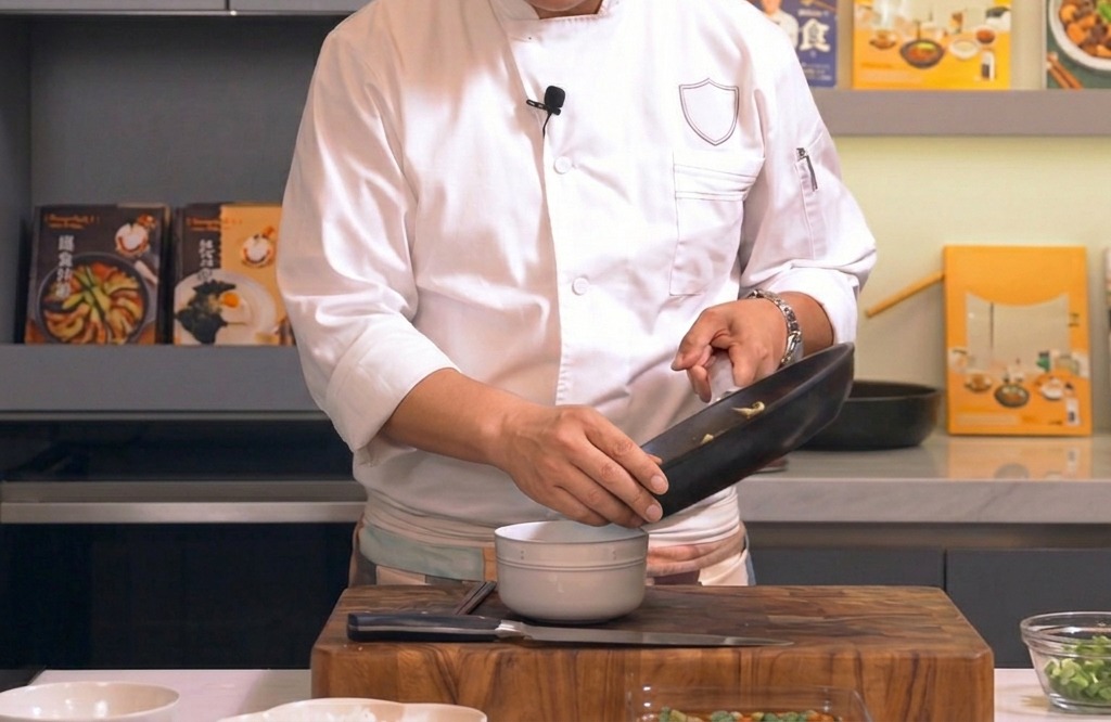 A mixture of sliced chicken and fluffy eggs being poured from a black frying pan over a bowl of steamed white rice.