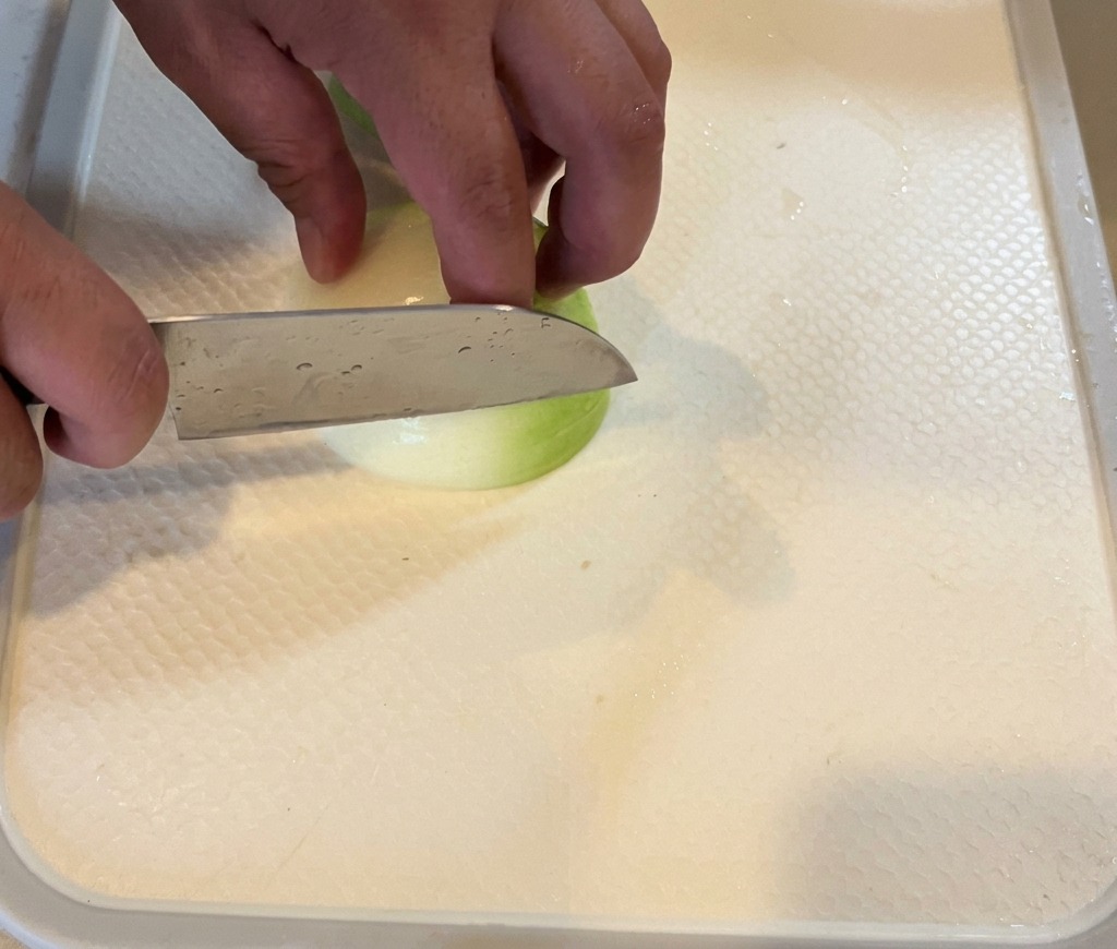 A person slicing a white onion into thin wedges on a white cutting board.
