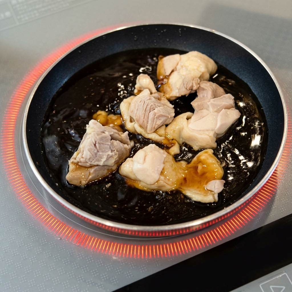 Blanched chicken pieces simmering in a bubbling dark brown sauce in a small round pan.