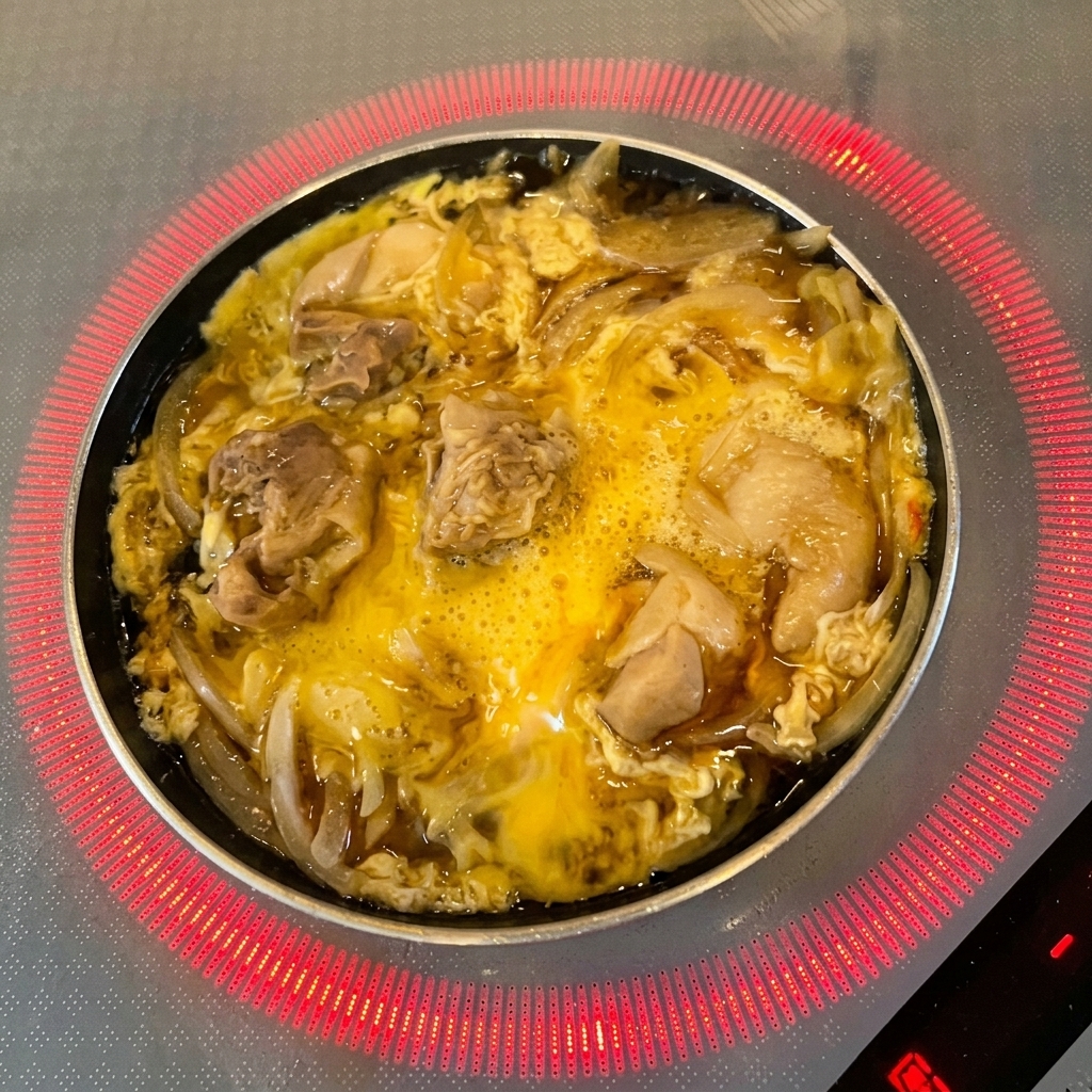 Fresh green mitsuba leaves being scattered over the partially cooked egg and chicken