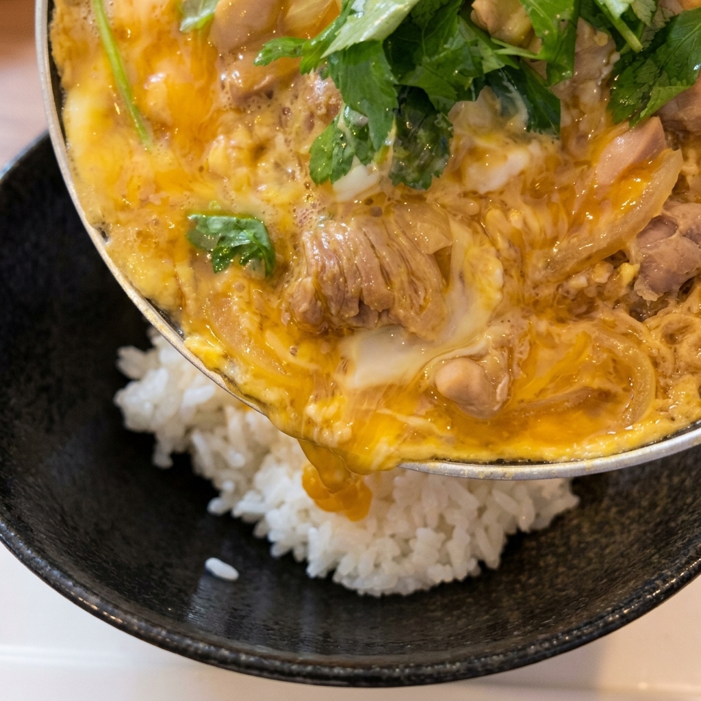 A pan being tilted to slide a cooked chicken and egg topping onto a bowl of fluffy white rice.