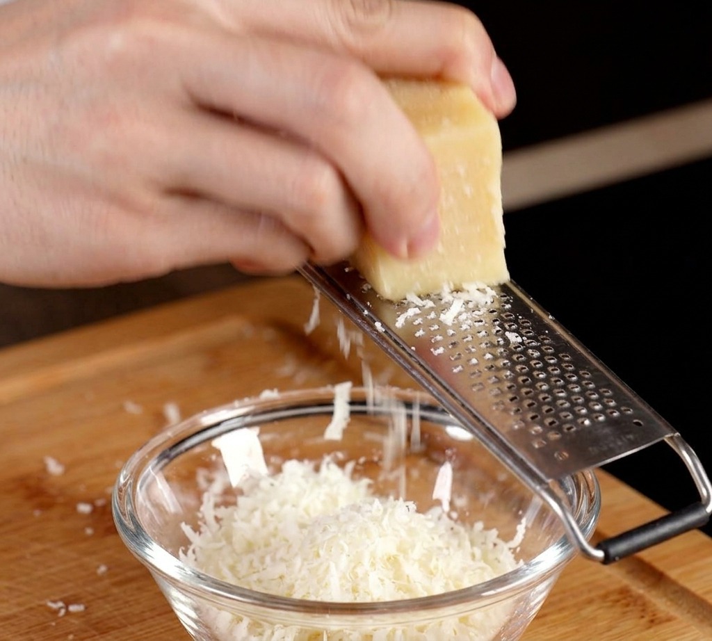 Grating a block of Parmesan cheese into a small bowl with a raw egg yolk.
