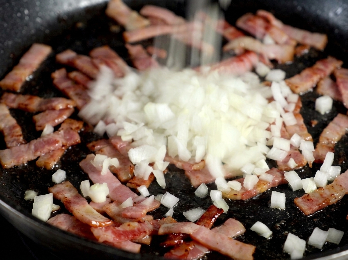 Minced white onions being sprinkled over a pan of sizzling cooked bacon strips.