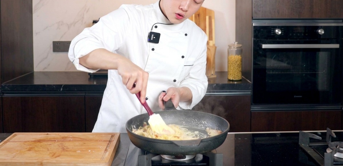 Chef stirring creamy pasta in a pan with a spatula to mix the sauce.
