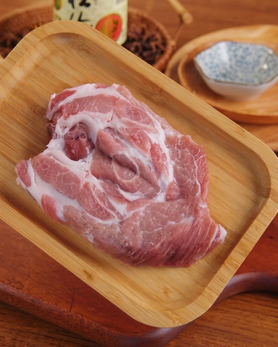 A flattened piece of raw marbled pork resting on a wooden tray after being pounded.