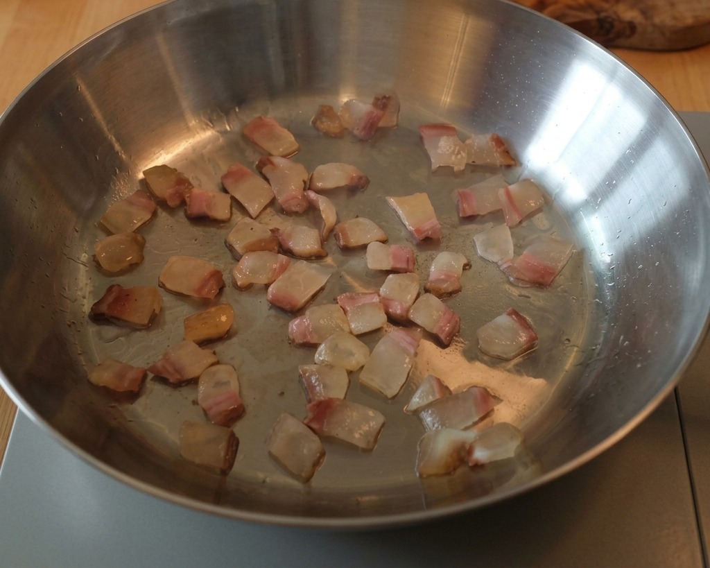 Guanciale cubes rendering in a metal skillet, with the fat turning into a clear liquid around the meat.