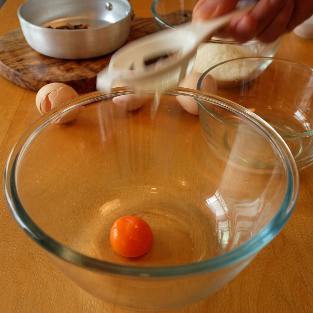 A single bright orange egg yolk sits in a clear glass bowl as the egg whites drip through a white separator tool.