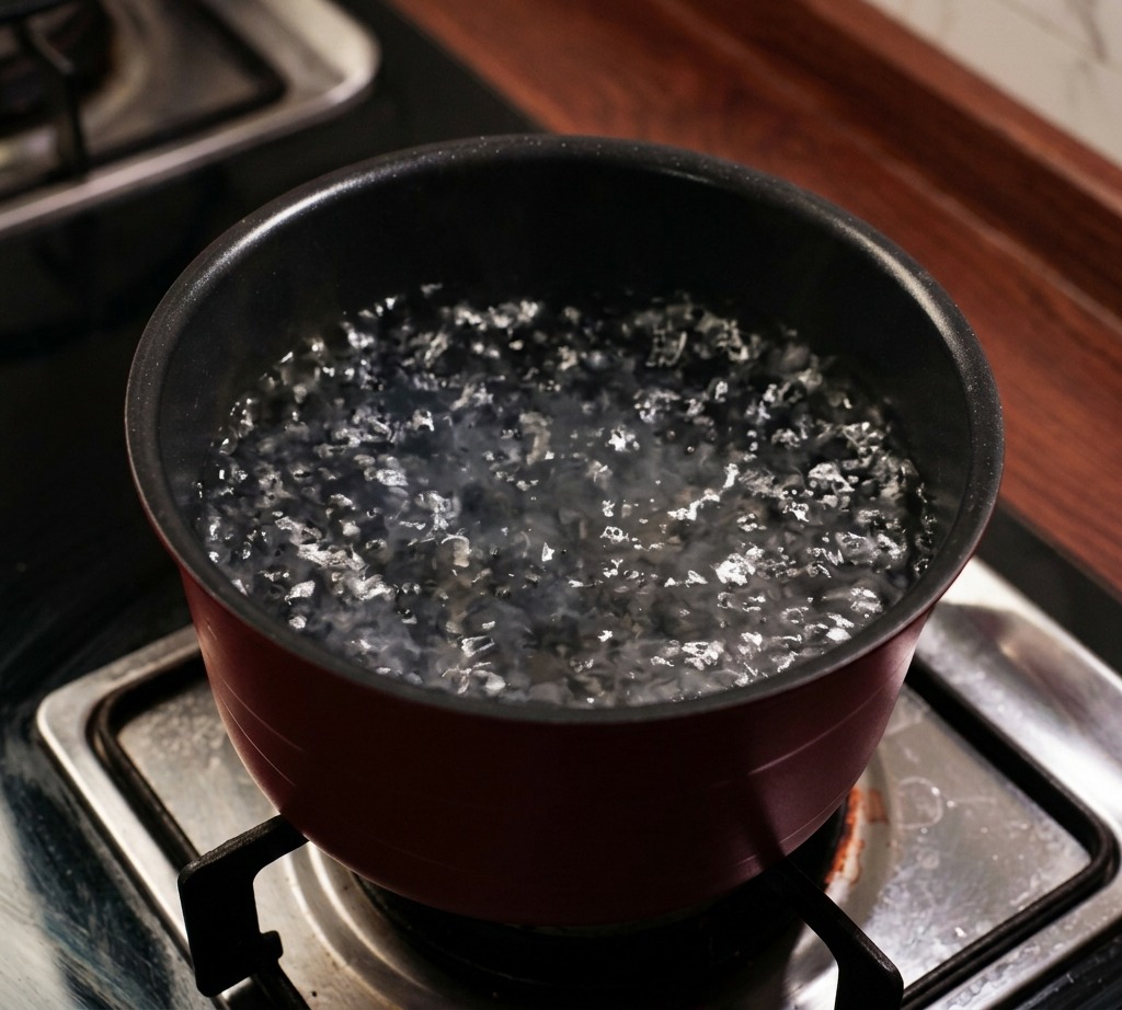 A dark red pot sitting on a gas stove filled with water at a rolling boil with steam rising.