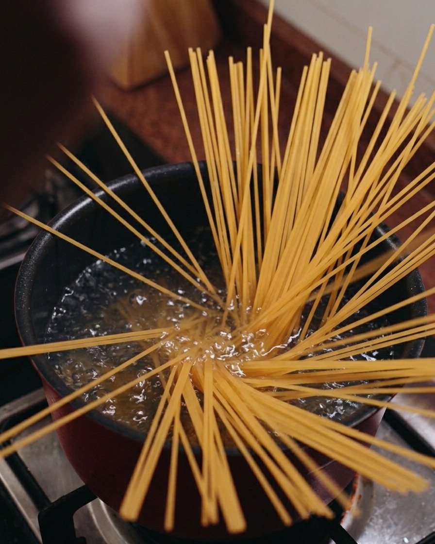 Dry spaghetti noodles standing vertically in a pot of boiling water, spreading out in a starburst pattern.