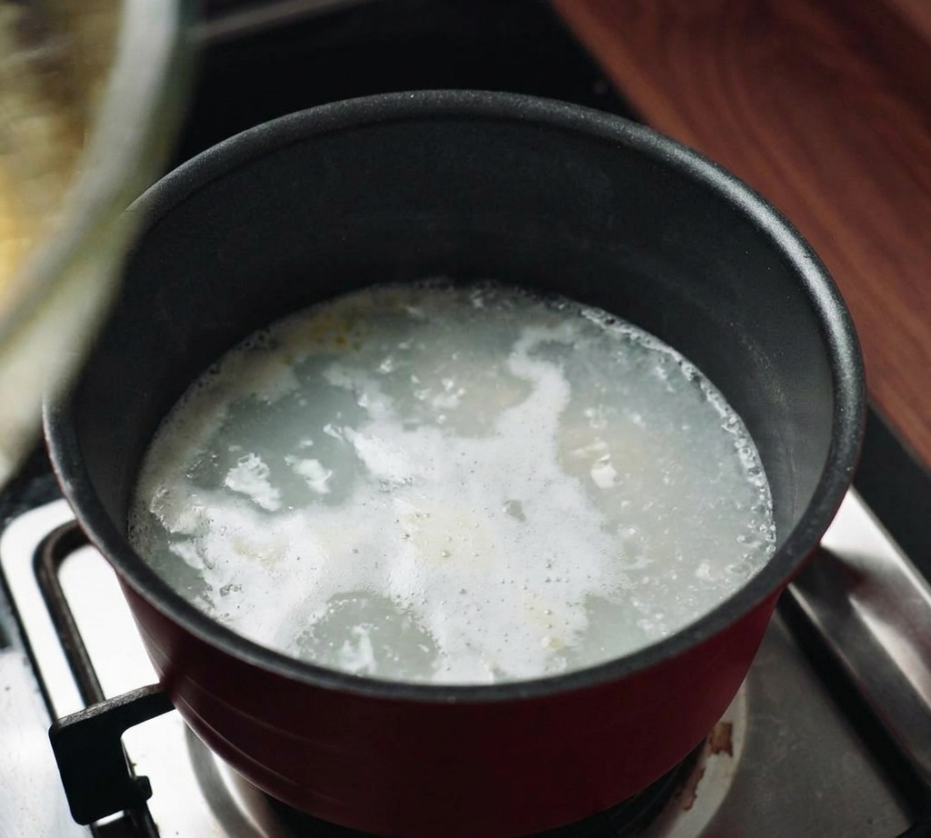 A glass mixing bowl being set on top of a pot of steaming water on a kitchen stove to create a double boiler.