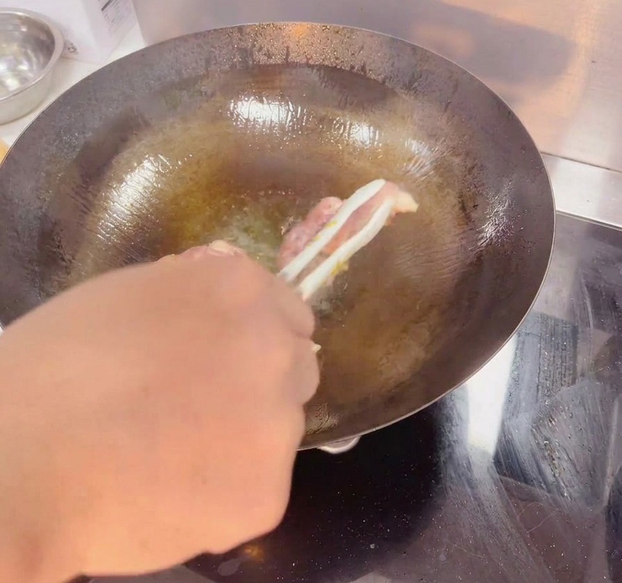 A pair of tongs flipping a chicken thigh in a dark wok to show the crispy golden brown skin.