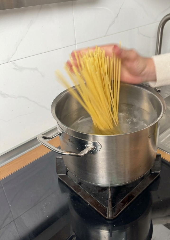 Dry pasta noodles being added to a pot of boiling water on an induction stove.