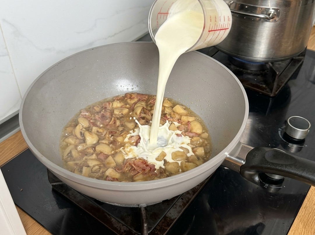 Heavy cream being poured into the pan, creating a splash as it hits the simmering mushroom base.