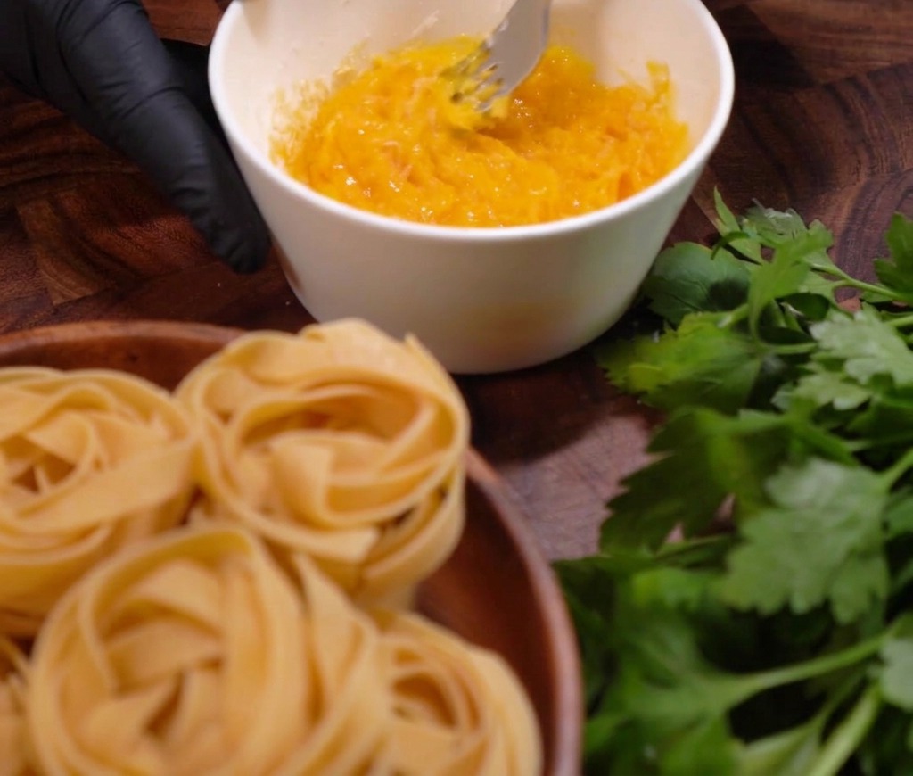 A person whisking egg yolks and grated cheese together with a fork in a white bowl to create a thick sauce base.