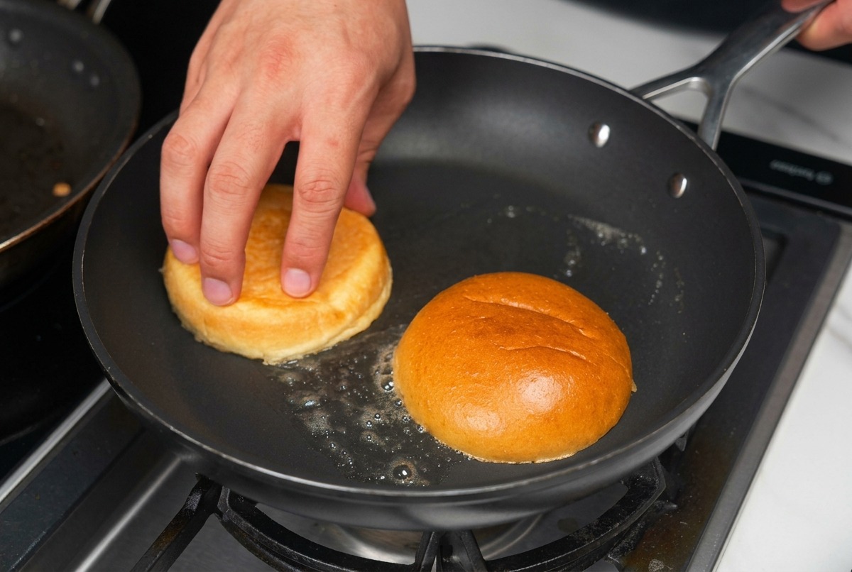 Burger bun halves being toasted face-down in a pan with bubbling melted butter.