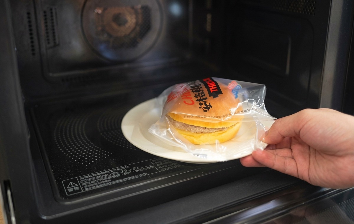 A hand placing the top half of a toasted brioche bun onto a burger topped with onions and melted cheese.