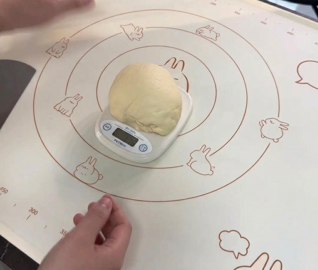 A large, smooth, round ball of dough sitting on a white digital kitchen scale on a patterned silicone baking mat.