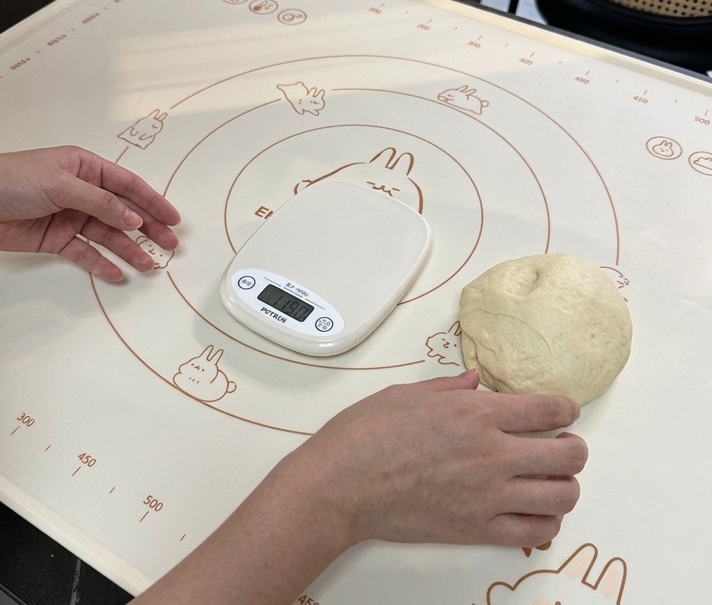 A small portion of dough resting on a baking mat next to a digital scale displaying its weight.