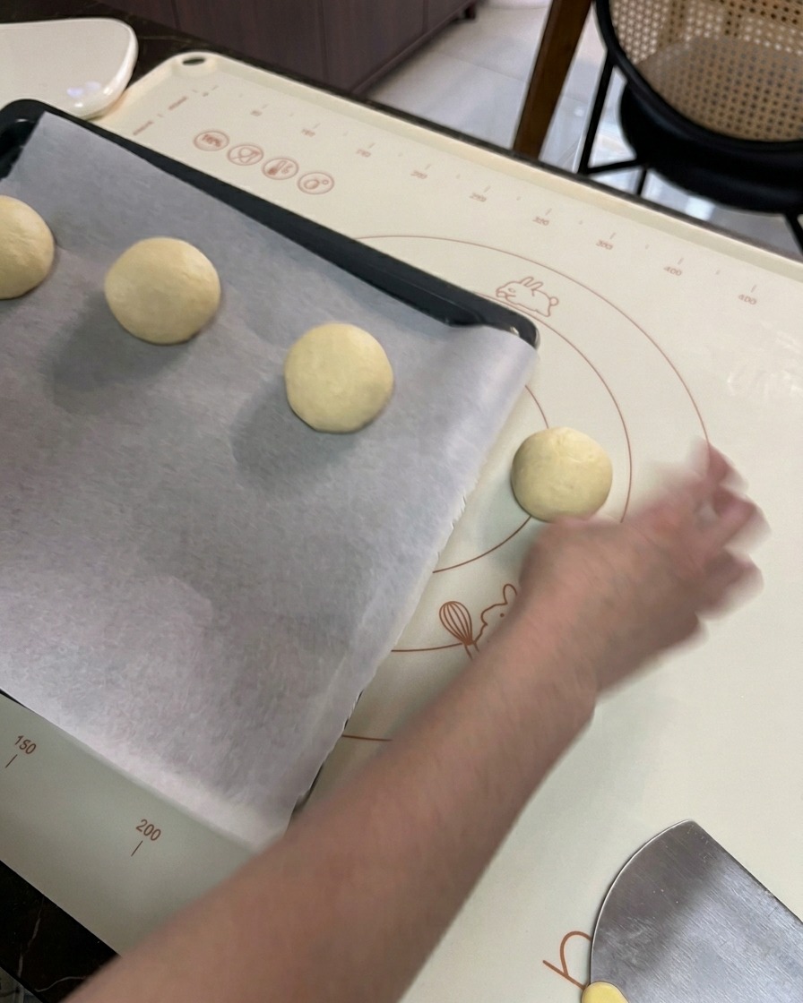 A hand placing shaped round dough balls onto a black baking sheet lined with white parchment paper.