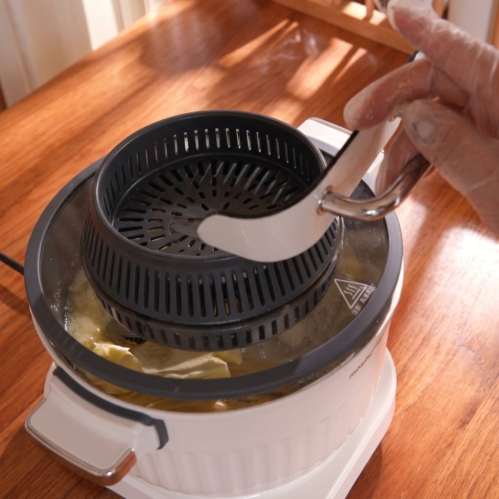 A hand holding a mixer attachment with a scoop of yellow softened butter, placing it into a bowl of dough.