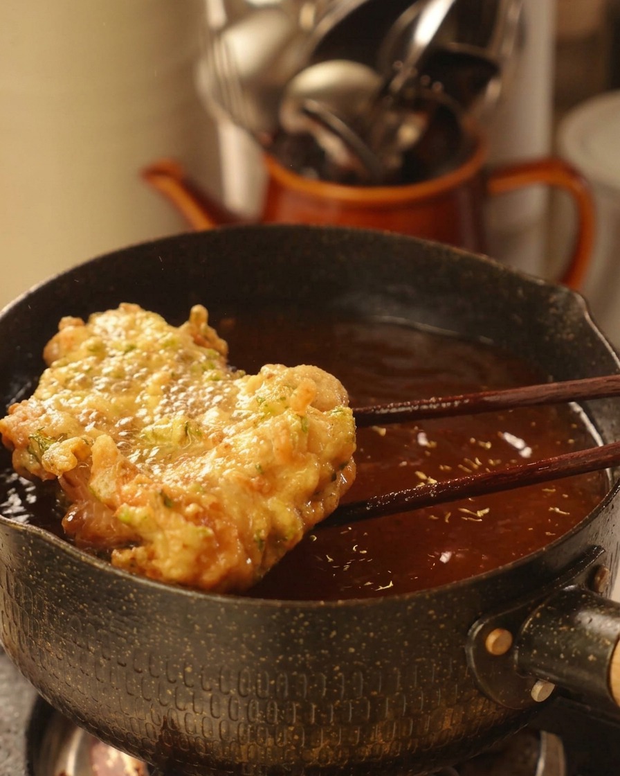 Lifting a large, golden-brown, crispy fried chicken patty out of hot oil using wooden chopsticks.