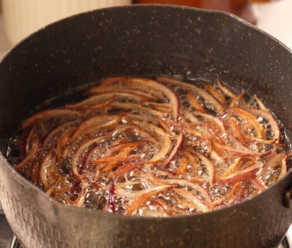Thin strips of red onion bubbling and frying in hot oil, turning a crispy golden brown.