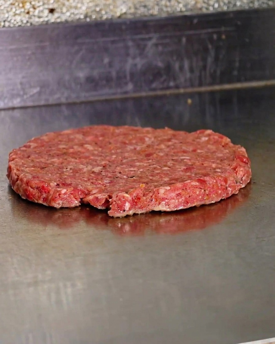 A freshly smashed, raw beef patty cooking on a hot metal griddle.