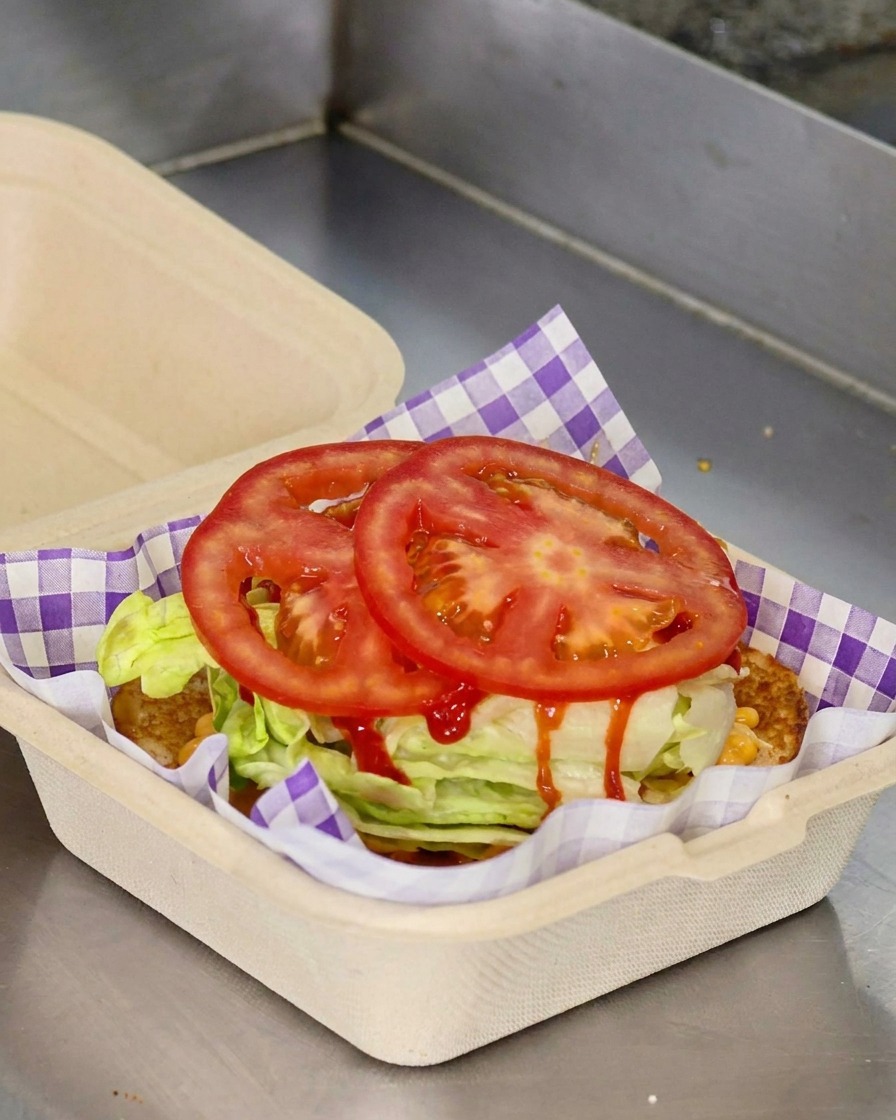 Two round slices of fresh red tomato placed on top of shredded lettuce in a paper takeout container.